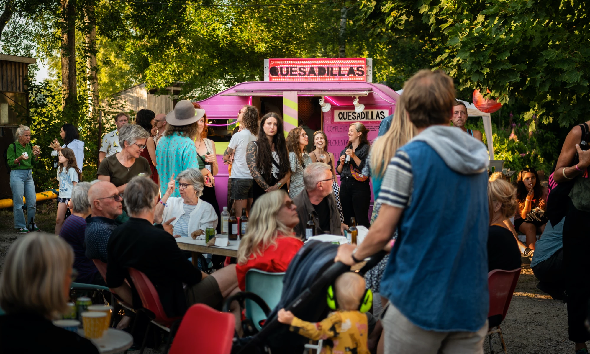 människor som umgås runt en rosa foodtruck och uteservering en sommarkväll.